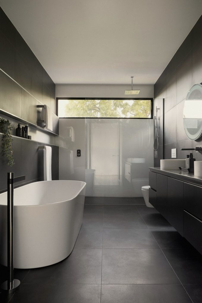 A sculptural stone bath and dark marble vanity in a monochrome bathroom.